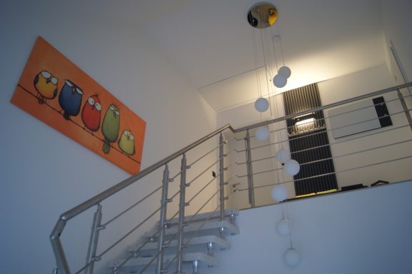 Blick von der Haustür auf das Treppenhaus zur Ferienwohnung, ein großes Bild mit Comicvögeln hängt links an der Wand.