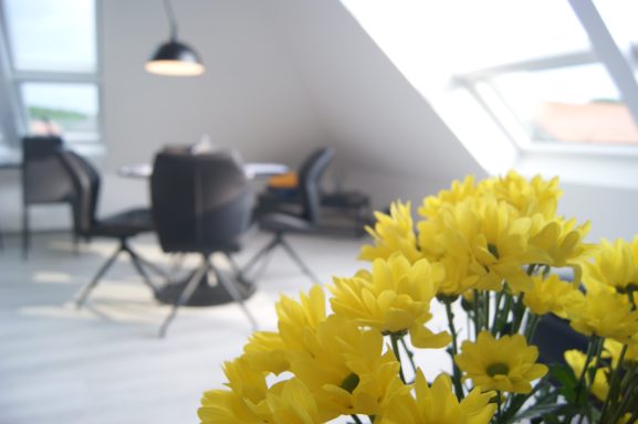 Gelbe Blumen im Vordergrund, im Hintergrund die Essecke für vier Personen