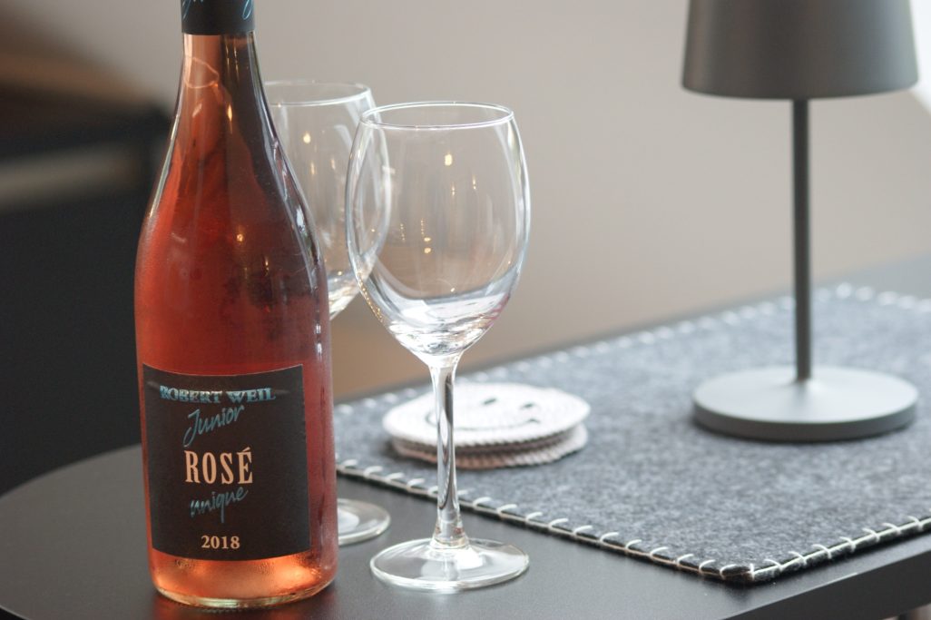 Eine Flasche Rosé, zwei Weingläser, Smilie-Untersetzer und eine kleine Lampe stehen auf einem Tresen in der Küche.