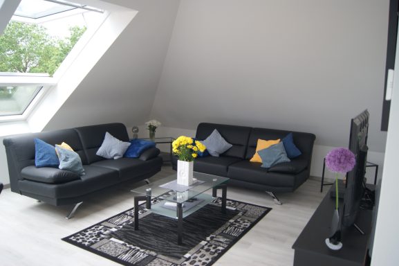 Blick auf die gemütliche Sofaecke mit großem Fernseher und großzügigen Fenstern