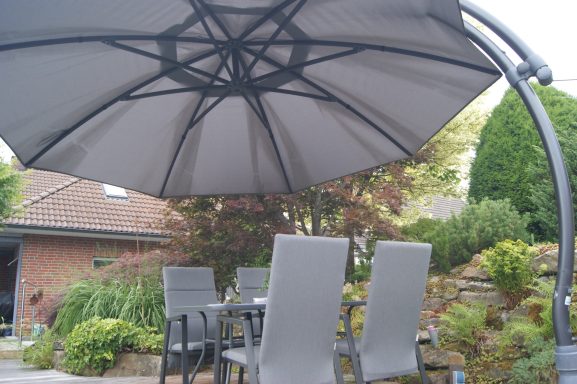 Die vier Stühle, der Tisch und der Sonnenschirm auf der Terrasse von der anderen Seite aus.