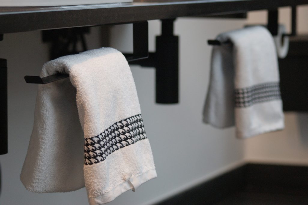 Zwei helle Handtücher mit schwarzen Details hängen unterhalb der Waschbecken.
