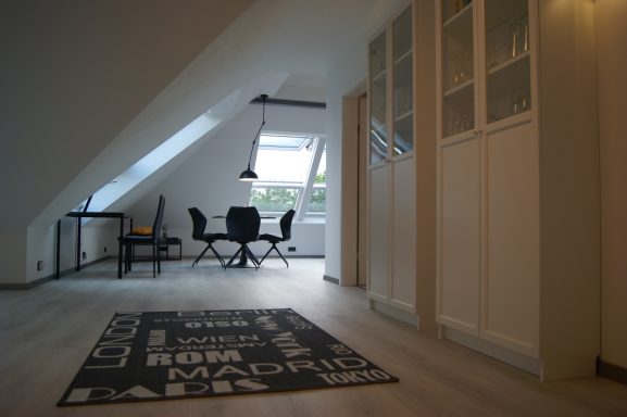 Im Vordergrund der Teppich, rechts der weiße hohe Schrank mit Gläsern und Büchern, im Hintergrund der Wohn- und Essbereich
