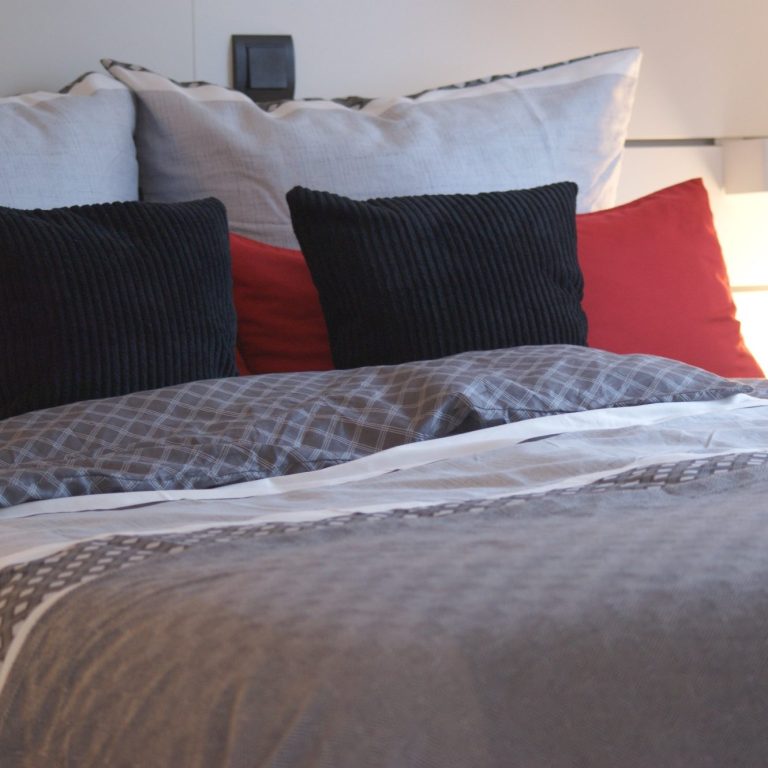 Frisch bezogenes Bett in einem der Schlafzimmer mit schwarzen, weißen und roten Kissen in unterschiedlichen Größen.